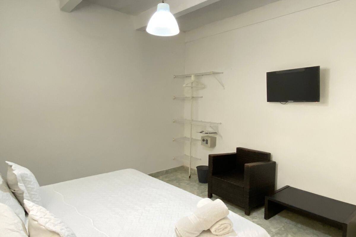 Un dormitorio con una cama, una silla, un televisor y una estantería.