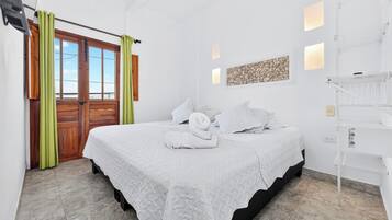 Un dormitorio con una cama, una puerta de madera, una ventana y una lámpara fijada a la pared.