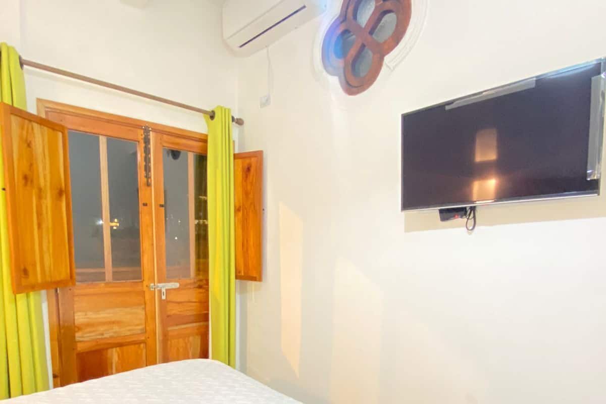 Un dormitorio con cama, televisor montado en la pared y ventana.