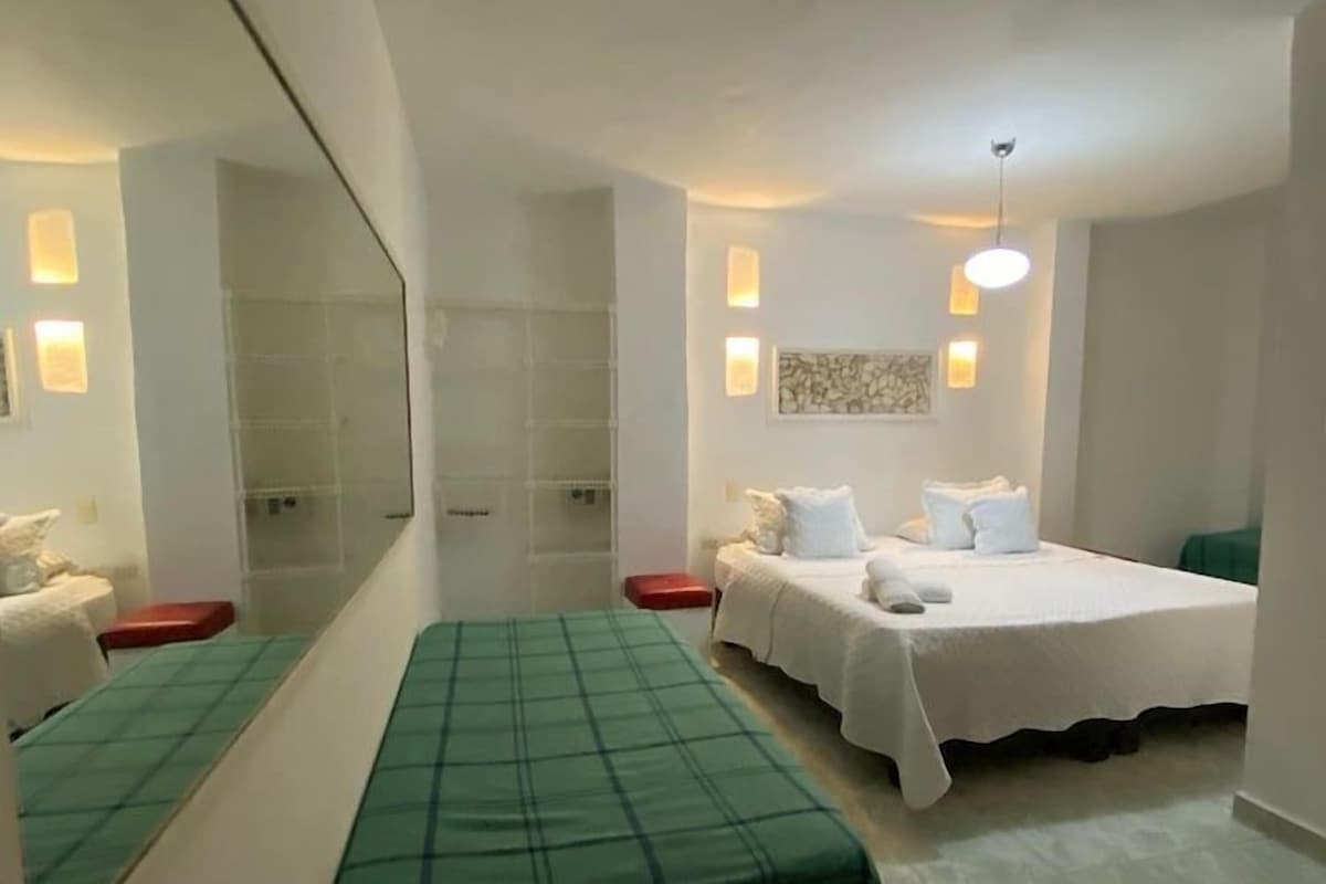 A hotel room with a bed, a bench, a mirror, and a wall-mounted light fixture.