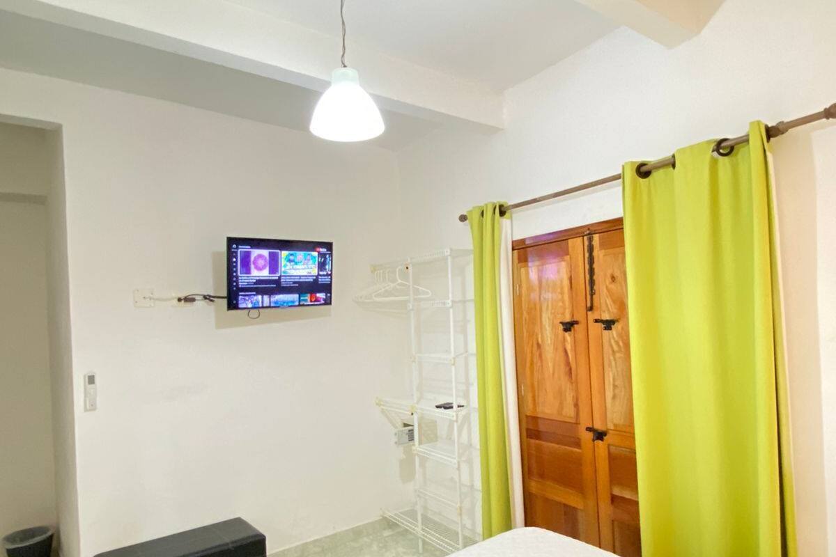 Un dormitorio con cama, televisor en la pared, armario de madera y cortina verde.