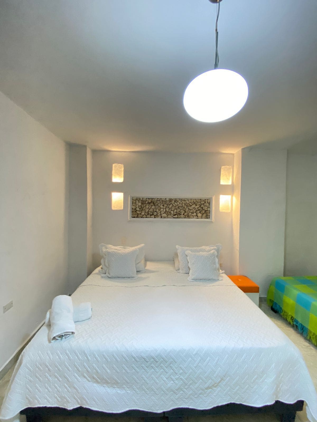 Un dormitorio ordenado con una cama grande, dos mesitas de noche, una obra de arte en la pared y una lámpara colgante.