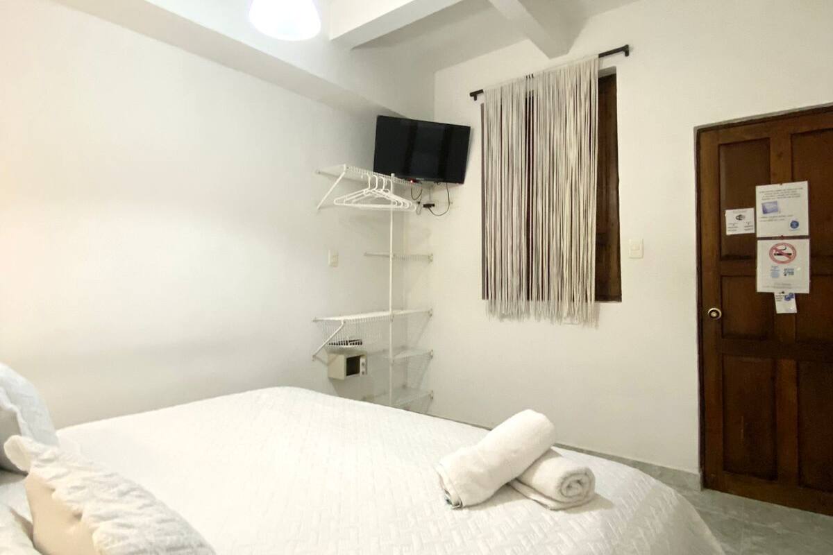 Habitación de hotel con cama, televisor montado en la pared, puerta de madera y toalla sobre la cama.