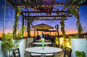 An outdoor patio with tables and chairs, a drink on one table, and string lights. - Le Foyer Arequipa (Arequipa)