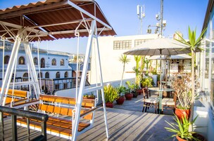 A rooftop terrace with wooden seating, potted plants, and a dining area with umbrellas.