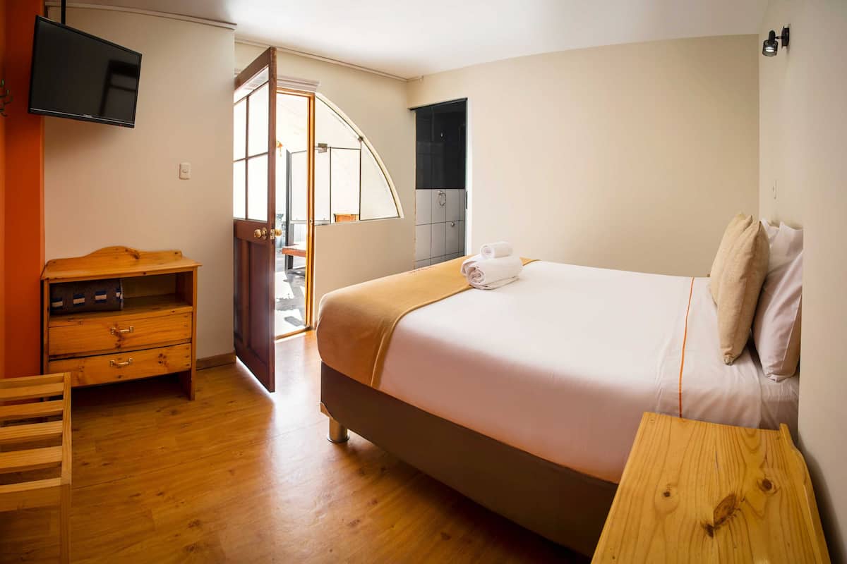 A bedroom with a bed, wooden dresser, and a television mounted on the wall.