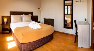A hotel room with a bed, a nightstand, a dresser, a mirror, and a small table with a plant.