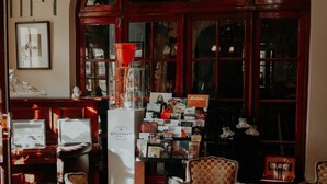 A cozy interior with wooden furniture, a large arched window, and a display of books and magazines. - Hotel Crystal Reims Centre (Reims)