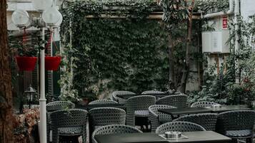 Un espace extérieur aménagé avec des tables et des chaises en osier, entouré de verdure et surmonté d’une pergola.