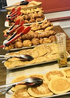 A buffet table with various pastries and flatbreads, including croissants and pancakes, with serving utensils.