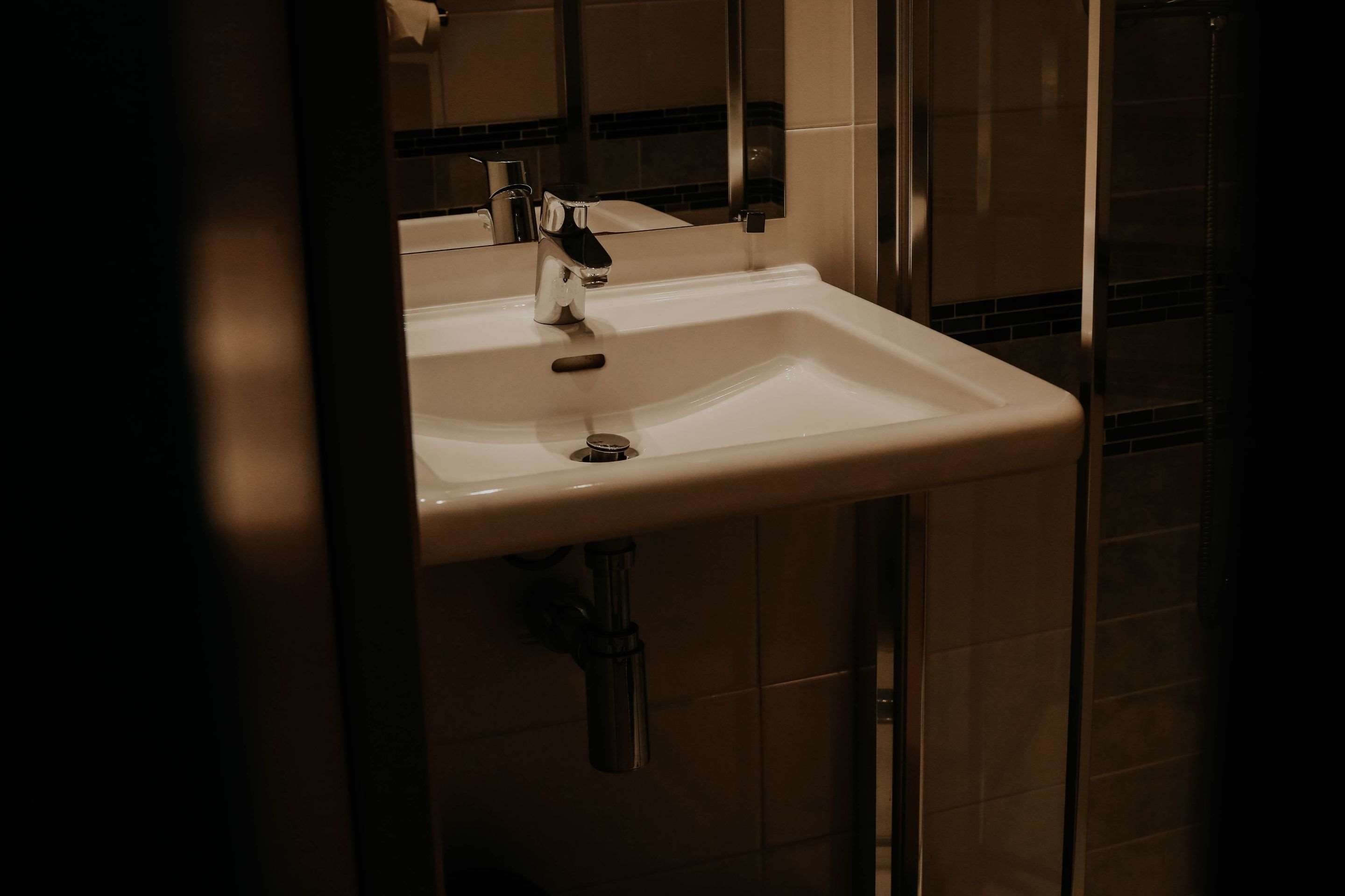 Un lavabo dans une salle de bain, avec un miroir au-dessus, un distributeur de serviettes et une zone de douche visible au fond.