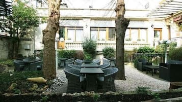 Un patio al aire libre con una mesa redonda y sillas, rodeado de árboles y un sendero de grava.