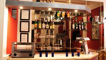 Angolo bar con scaffali pieni di bottiglie di liquori, bicchieri e una macchina da caffè.