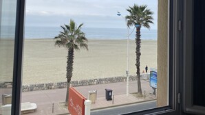 A view from a window overlooking a beach with palm trees and a sign for a hotel.