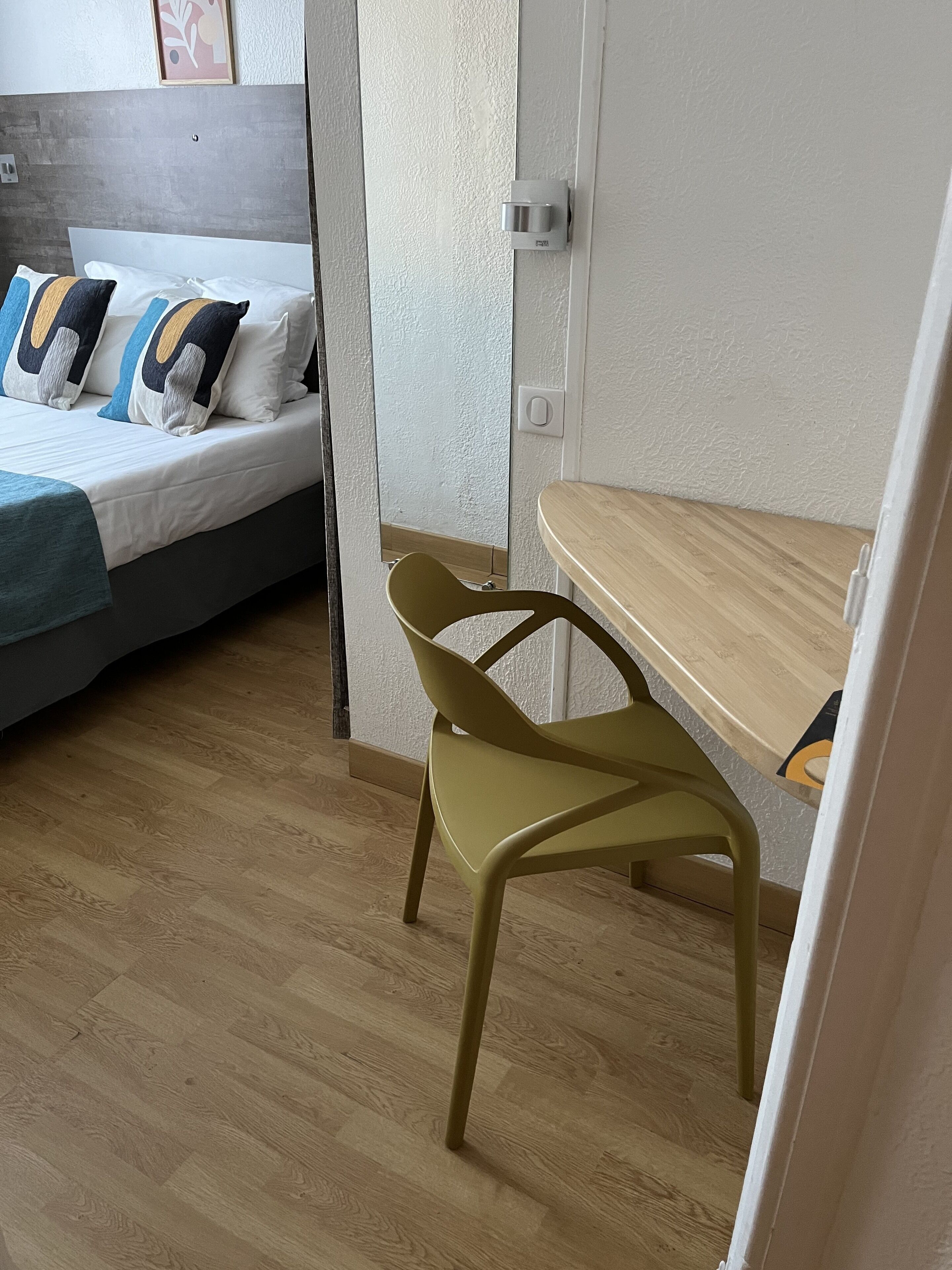 A hotel room with a bed, a desk, a chair, and a wooden floor.