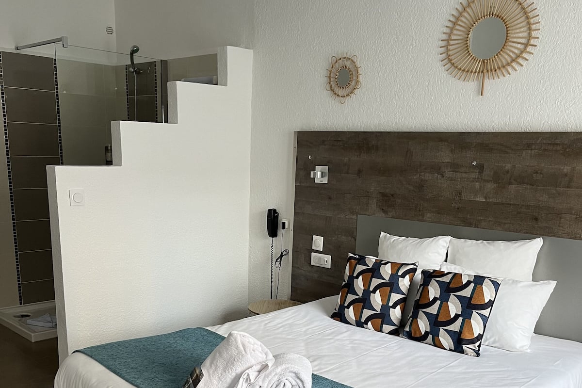 A modern hotel room with a large bed, a wooden headboard, and a bathroom with a glass shower enclosure.