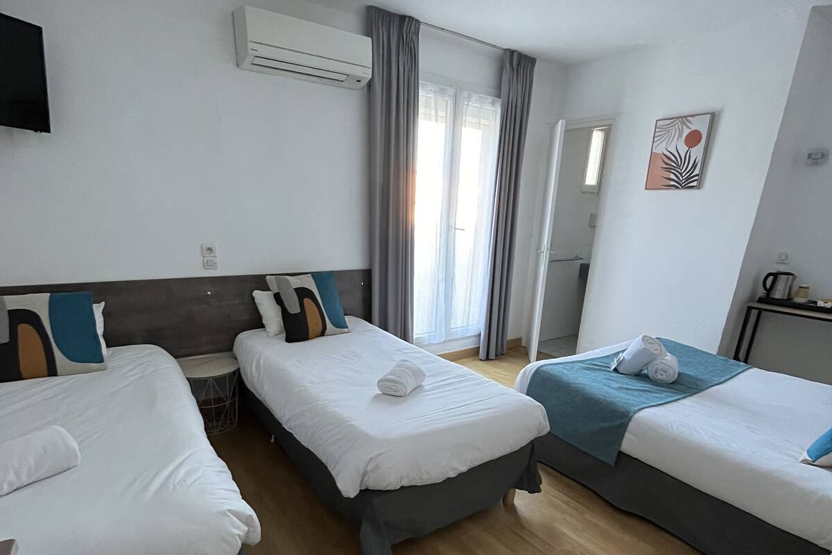 A hotel room with three single beds, a flat-screen TV, an air conditioning unit, and a window with curtains.