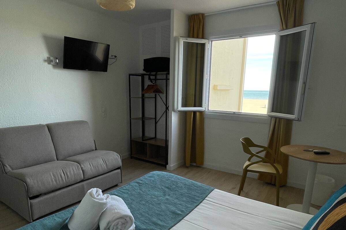 A hotel room with a bed, a sofa, a TV, a window with curtains, and a small table.