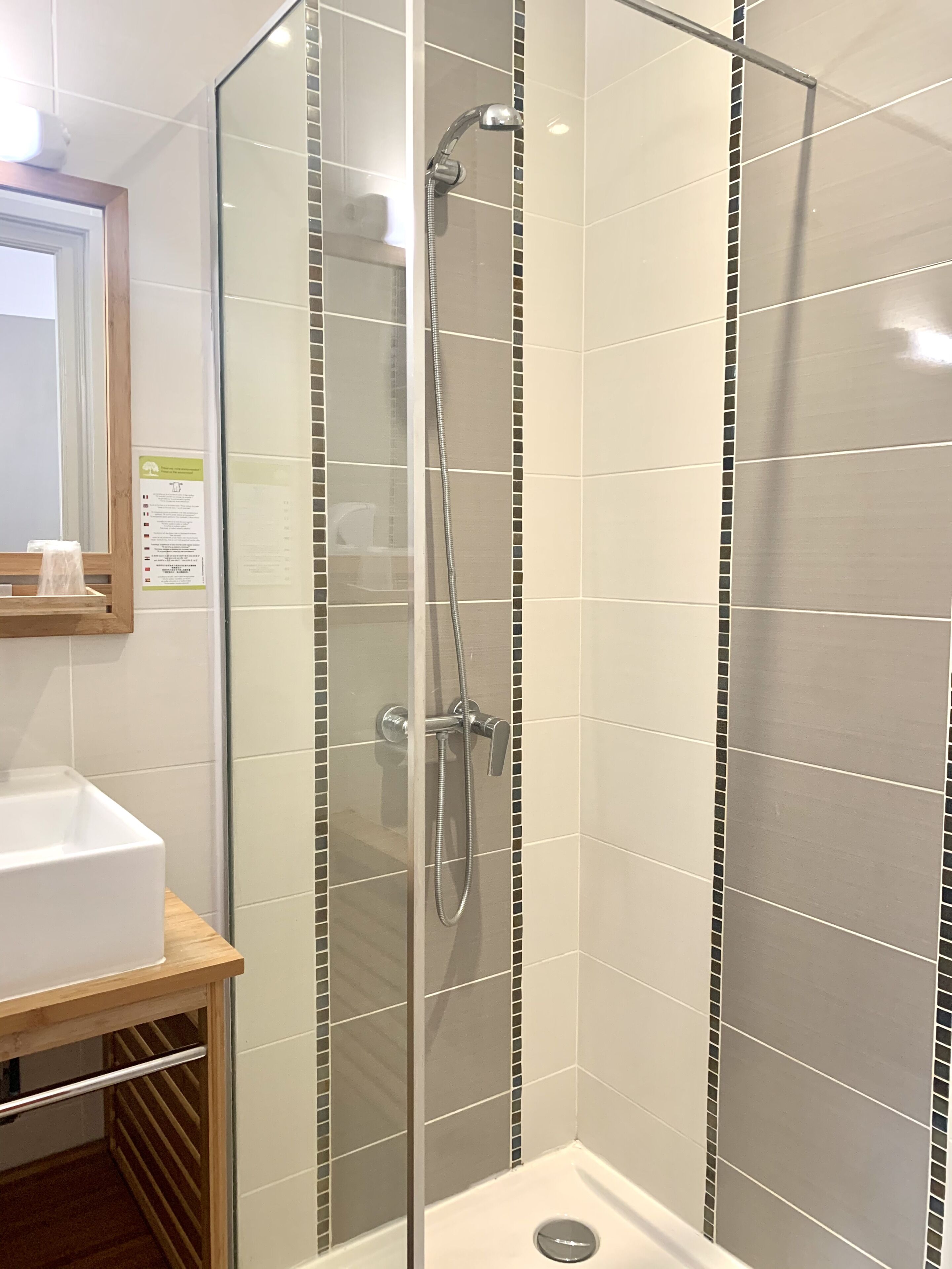 A glass-enclosed shower stall with a handheld showerhead and a wall-mounted faucet.