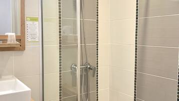 A glass-enclosed shower stall with a handheld showerhead and a wall-mounted faucet.