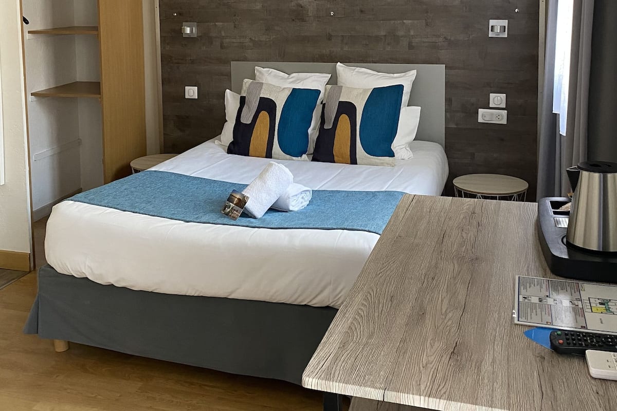 A hotel room with a bed, bedside table, and a small table with a kettle.
