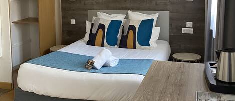 Una habitación de hotel con una cama, una mesita de noche y una pequeña mesa con una tetera.