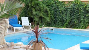 A pool area with a blue pool, white lounge chairs, and a potted plant.