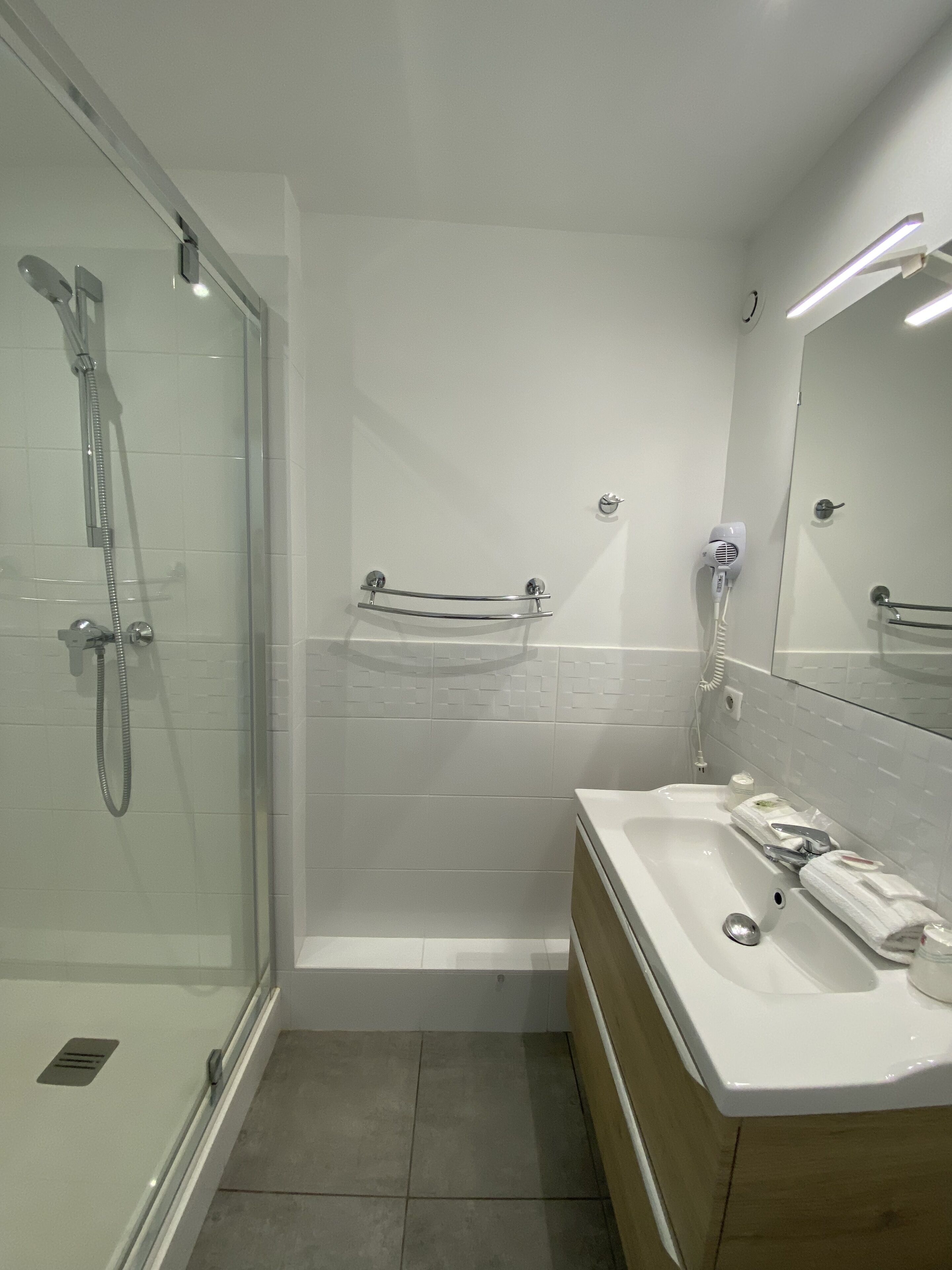 A modern bathroom with a glass-enclosed shower, a white bathtub, and a wooden vanity.