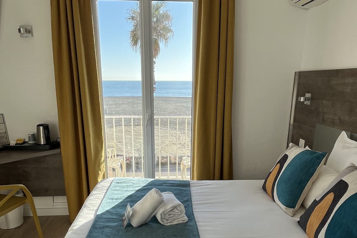 A hotel room with a bed, a desk, and a view of the beach.