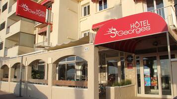 A hotel with a red awning, multiple balconies, and large windows.