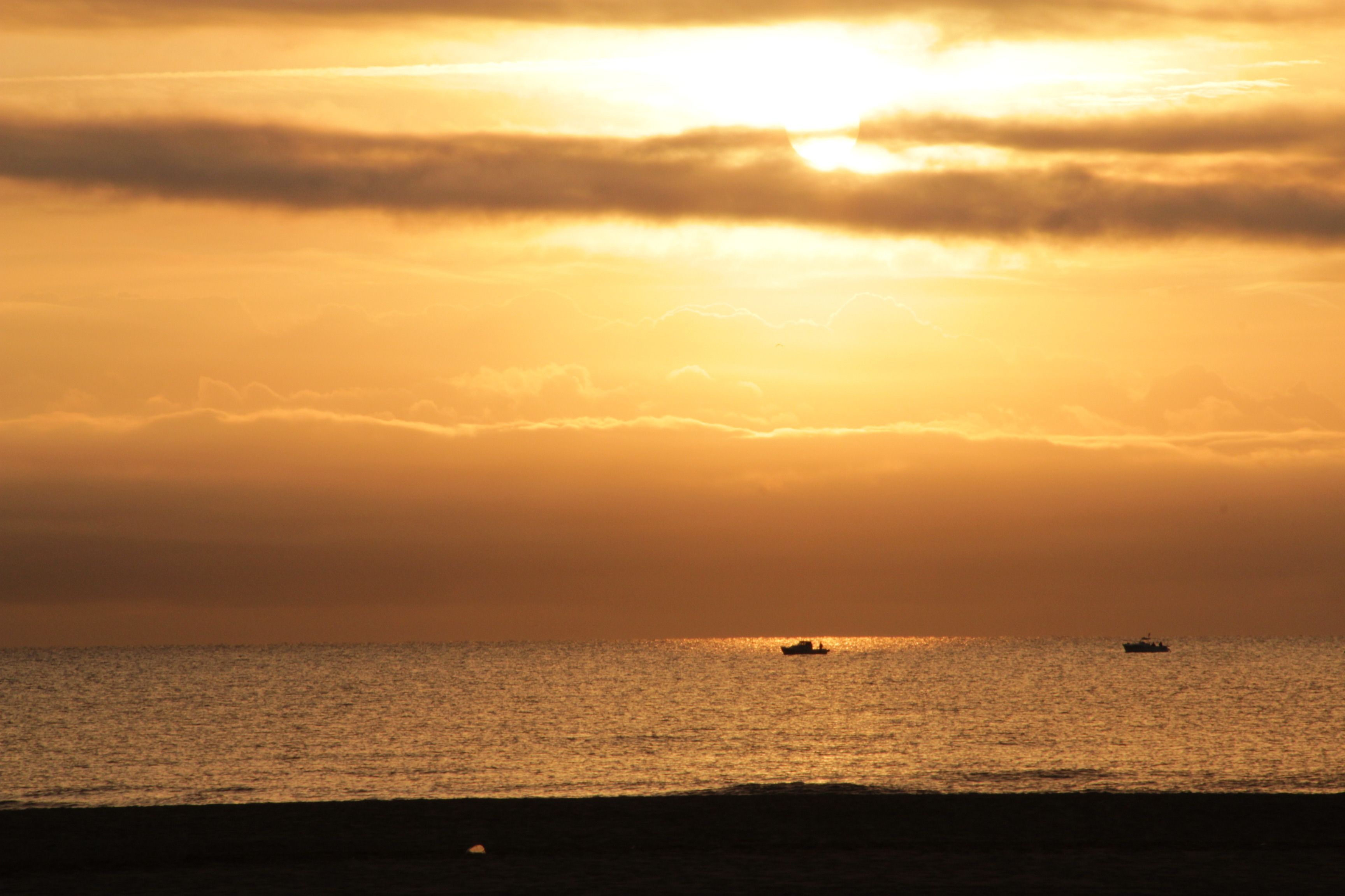 Un coucher de soleil sur une mer calme, avec deux bateaux visibles.