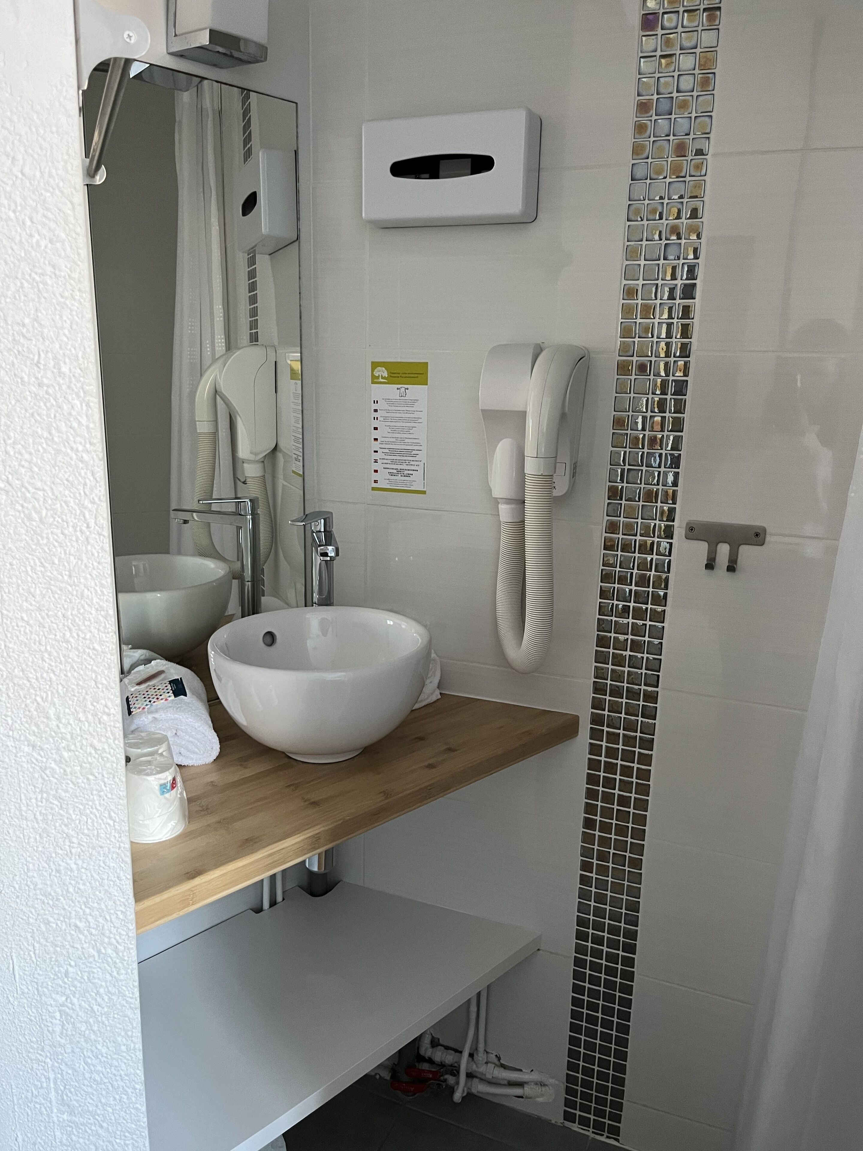 A modern bathroom with a large white sink, a mirror, a handheld showerhead, and a wall-mounted phone.