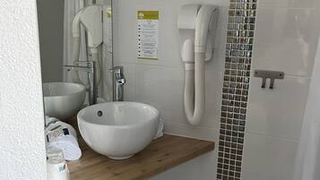 A modern bathroom with a large white sink, a mirror, a handheld showerhead, and a wall-mounted phone.