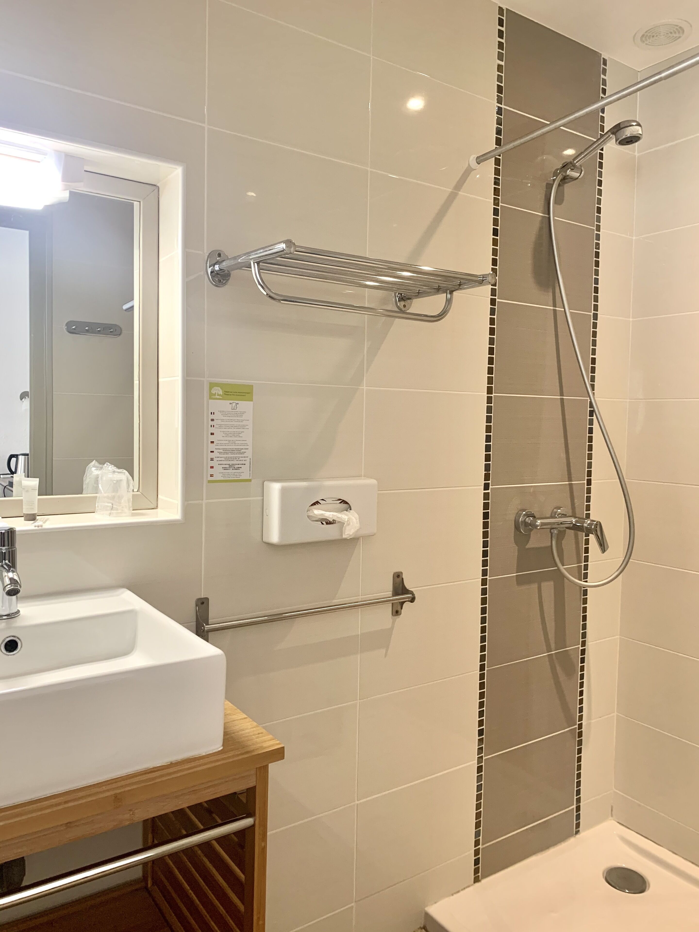 A bathroom with a sink, mirror, towel dispenser, and shower with a handheld showerhead.