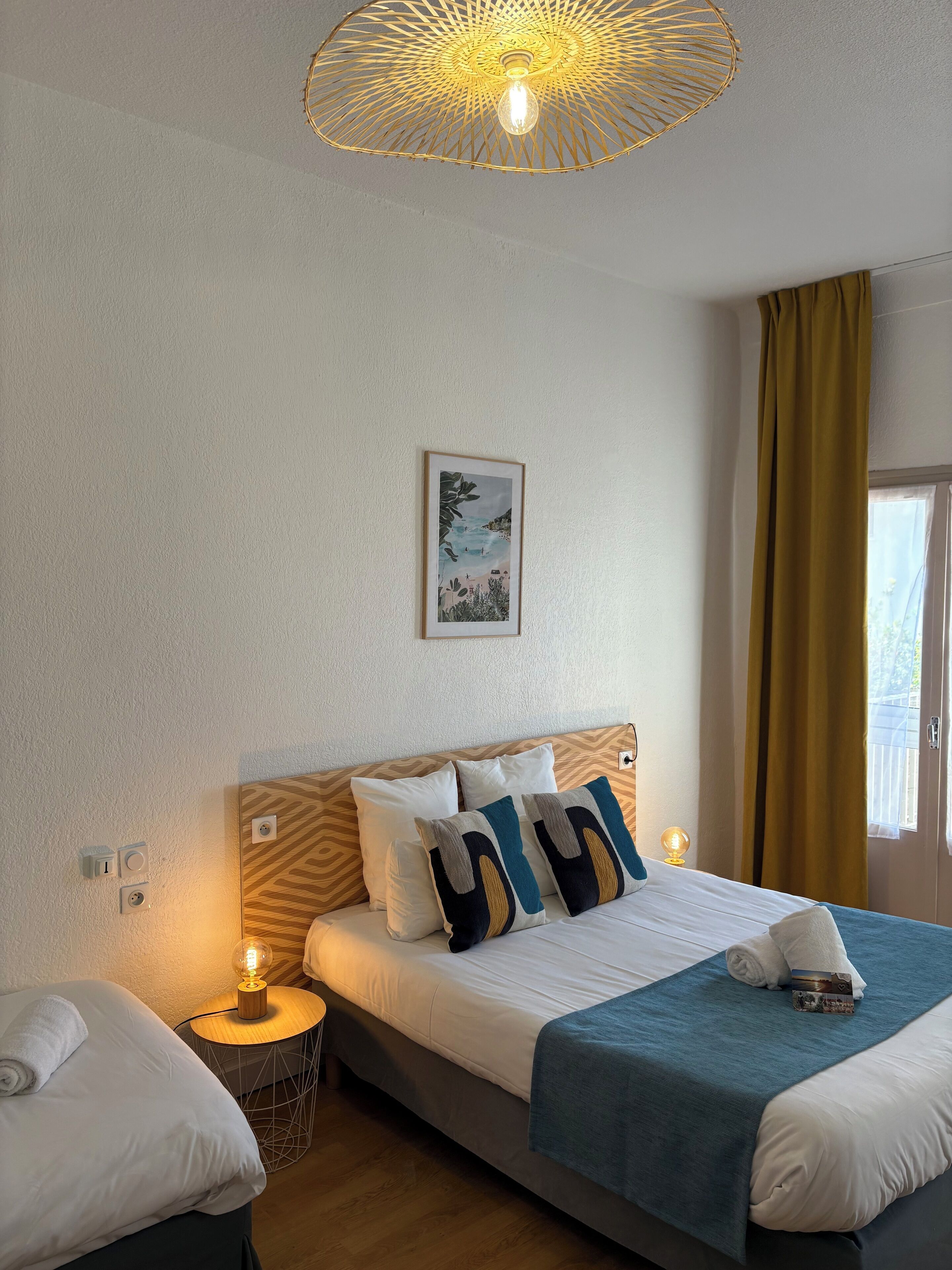 Habitación de hotel ordenada con cama, lámparas de noche, un cuadro en la pared y una ventana con cortinas.
