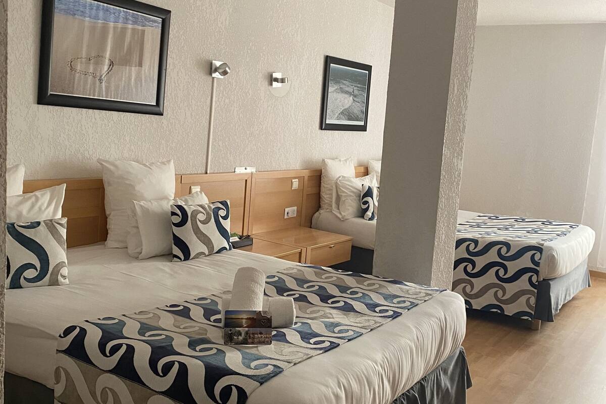 A hotel room with two beds, each with a patterned bedspread, a nightstand, and a wall-mounted lamp.