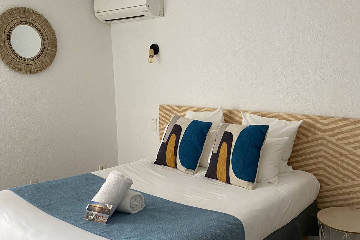 A neatly made bed with a blue and white bedspread, two pillows with blue and yellow stripes, and a rolled towel on the bed.