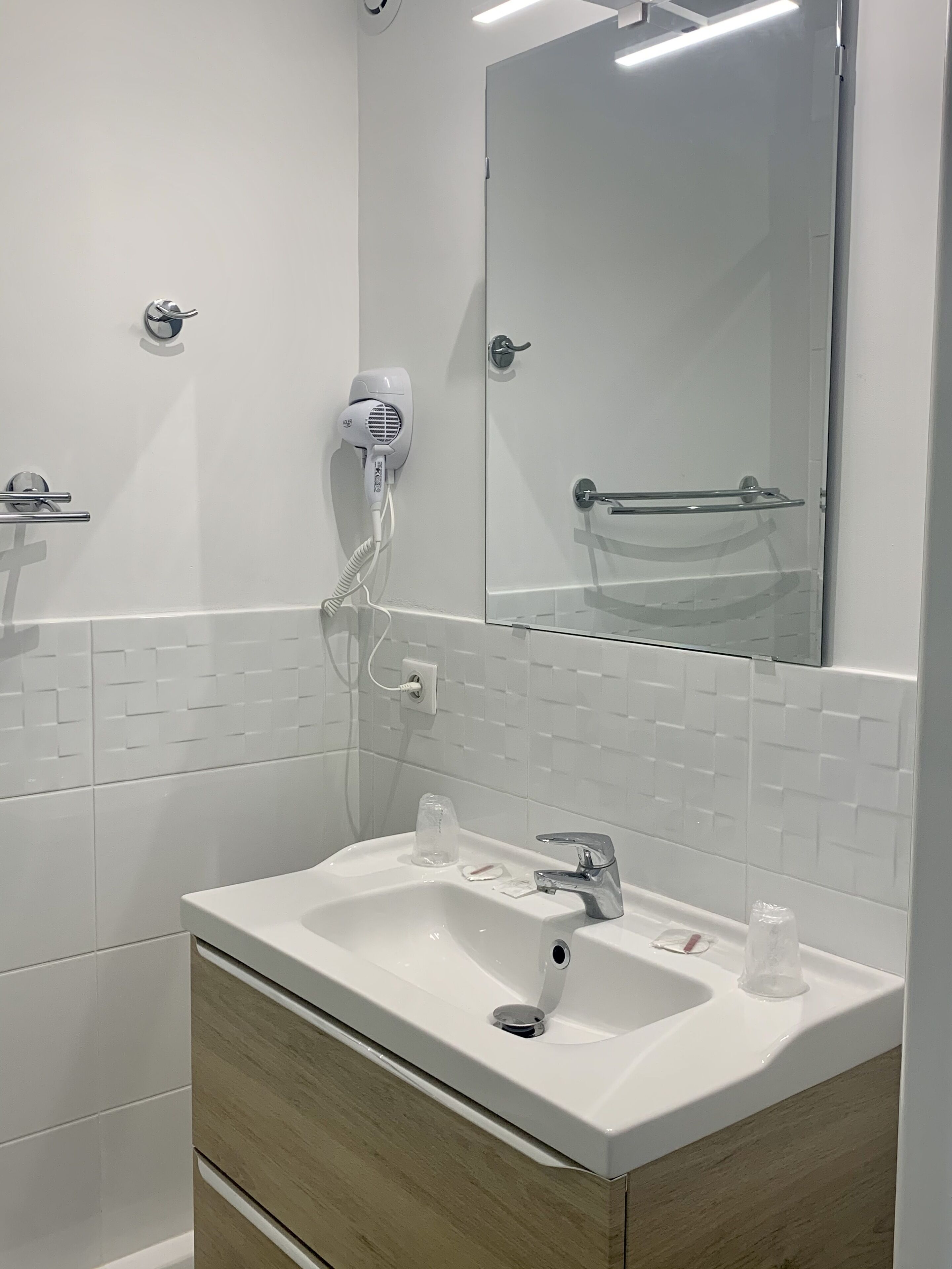 A modern bathroom with a white sink, a mirror, and a hairdryer mounted on the wall.