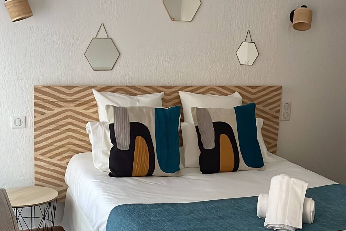 A neatly made bed with a blue blanket and multiple pillows, a wooden headboard, and geometric wall sconces.