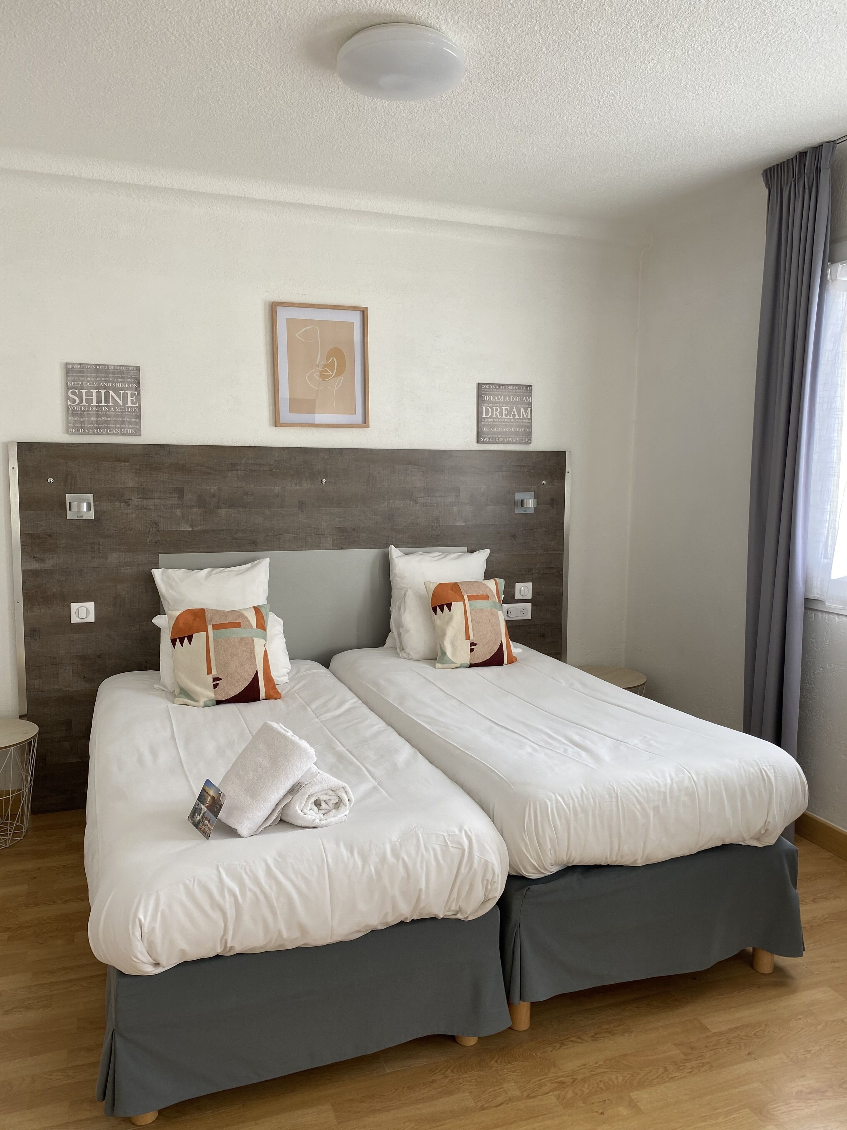 Ein Hotelzimmer mit zwei Einzelbetten, einem hölzernen Kopfteil, einem gerahmten Motivationszitat und einem kleinen runden Tisch.