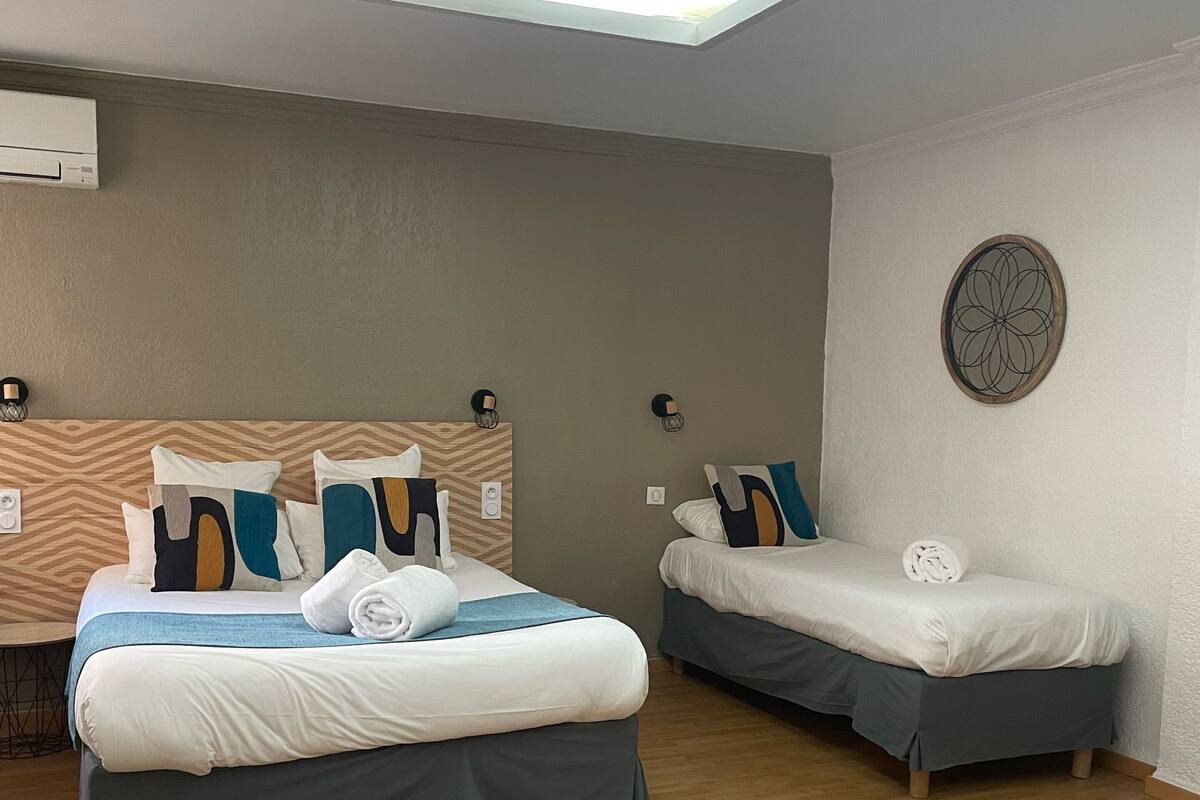 A modern hotel room with two beds, a ceiling light, a wall-mounted air conditioner, and a decorative wall piece.