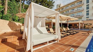 Zona junto a la piscina con una cama con dosel, sillones de descanso y una pileta.