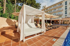 Una piscina al aire libre, sombrillas, sillones reclinables de piscina