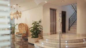 Un hall con una silla de madera, plantas en macetas, una escalera y una puerta.