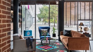 Una sala de estar moderna con sofá, sillón y mesa de centro, un ventanal con persianas y vistas a la calle.