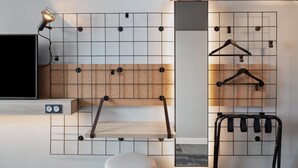 Una habitación moderna con una pared de diseño en cuadrícula, un televisor montado, un estante de madera, un perchero y un otoman blanco.