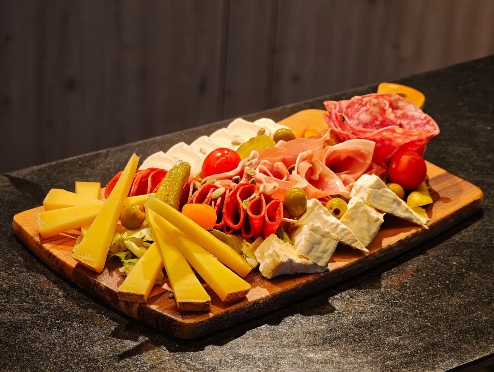 A wooden board with various cheeses, meats, and vegetables.