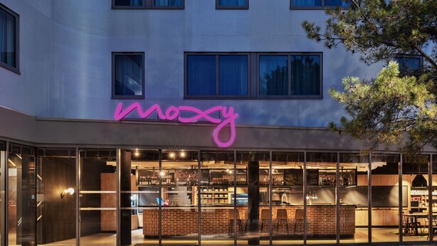 Un edificio moderno con un letrero de neón que dice "moscy" y un bar visible a través de amplios ventanales.