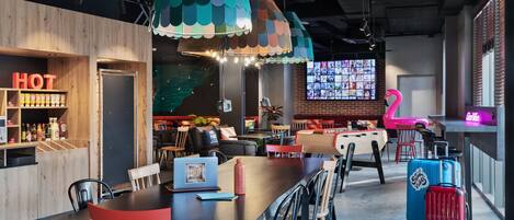 A modern lounge area with a long table, chairs, a neon flamingo sign, and a colorful rug.