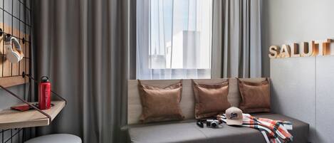 Una habitación de hotel moderna con una cama, una mesita de noche con una botella de agua roja, una cámara y un gorro.